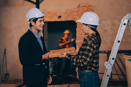 Construction manager and engineer dressed in orange work vests and hard helmets explore construction documentation on the building site near the steel framesの写真素材