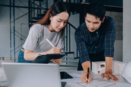 Construction manager and engineer dressed in orange work vests and hard helmets explore construction documentation on the building site near the steel framesの写真素材