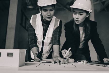 Construction manager and engineer dressed in orange work vests and hard helmets explore construction documentation on the building site near the steel framesの写真素材