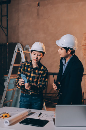 Construction manager and engineer dressed in orange work vests and hard helmets explore construction documentation on the building site near the steel framesの写真素材