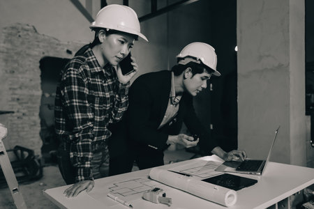 Construction manager and engineer dressed in orange work vests and hard helmets explore construction documentation on the building site near the steel framesの写真素材