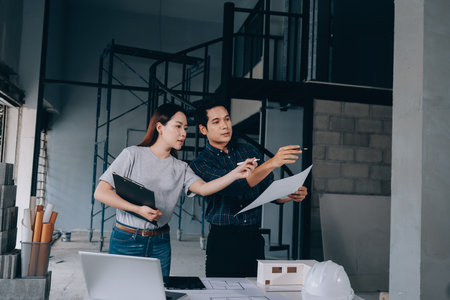Construction manager and engineer dressed in work vests and hard helmets explore construction documentation on the building site near the steel framesの写真素材