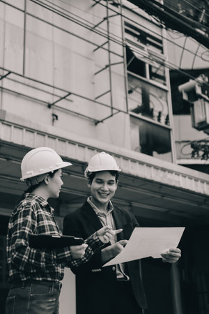 Construction manager and engineer dressed in hard helmets explore construction documentation on the building site near the steel framesの写真素材