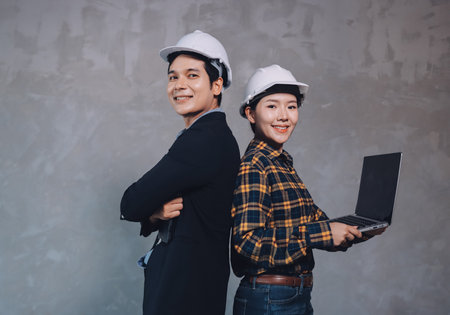 Construction manager and engineer dressed in orange work vests and hard helmets explore construction...