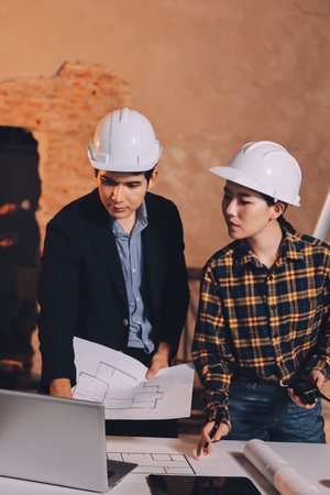 Construction manager and engineer dressed in orange work vests and hard helmets explore construction...