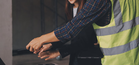 Construction manager and engineer dressed in orange work vests and hard helmets explore construction documentation on the building site near the steel framesの写真素材