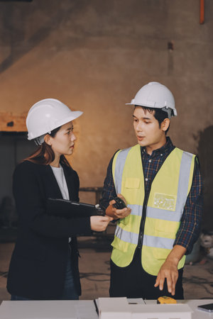 Construction manager and engineer dressed in work vests and hard helmets explore construction...