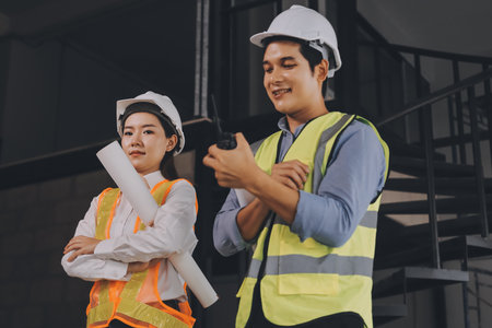Construction manager and engineer dressed in orange work vests and hard helmets explore construction...