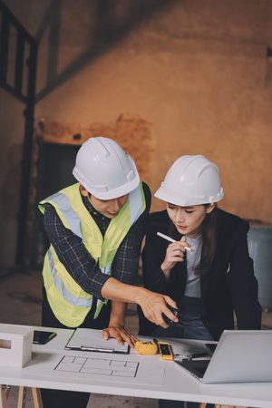 Construction manager and engineer dressed in orange work vests and hard helmets explore construction...