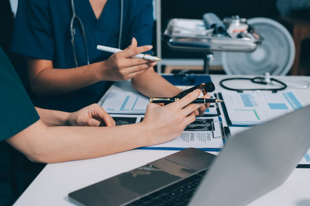 Two doctors and a female nurse meet at a table in the hospital, collaborating on medical tasks using...