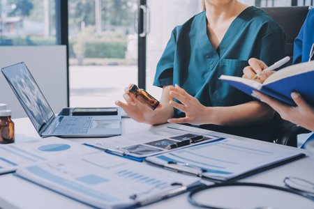 Two doctors and a female nurse meet at a table in the hospital, collaborating on medical tasks using...