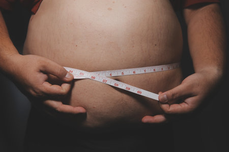 Fat man in front of a mirror looks at his body. Excess belly fat, Unhealthy lifestyle, Diet concept.の写真素材