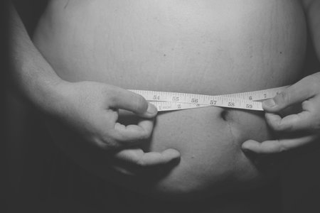 A person is measuring their belly with a tape measure.の写真素材