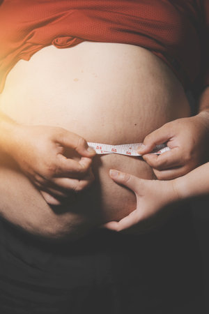 Asian man in front of a mirror looks at his body. Excess belly fat, Unhealthy lifestyle, Diet concept.の写真素材