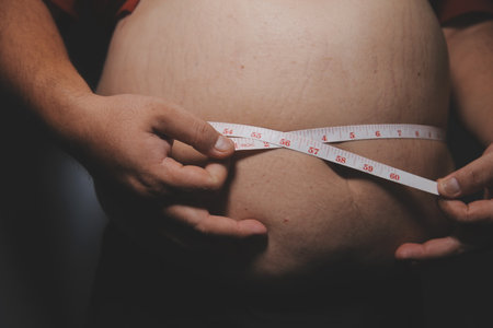 Asian man in front of a mirror looks at his body. Excess belly fat, Unhealthy lifestyle, Diet concept.の写真素材