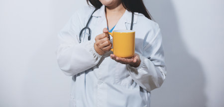 Portrait of Asian doctor woman standing holding coffee cup in white studio backgroundの写真素材