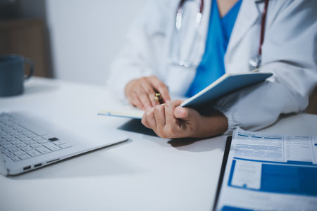 Middle aged female doctor working on laptop in doctor's roomの写真素材