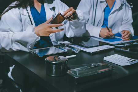 Two doctors and a female nurse meet at a table in the hospital, collaborating on medical tasks using...