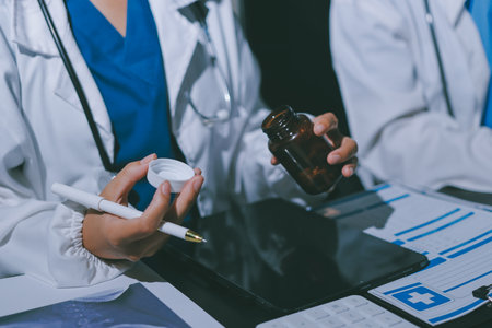 Two doctors and a female nurse meet at a table in the hospital, collaborating on medical tasks using laptops and computersの写真素材
