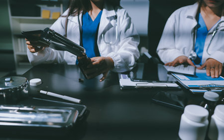 Two doctors and a female nurse meet at a table in the hospital, collaborating on medical tasks using...