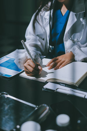 Two doctors and a nurse meet at a table, collaborating on tasks using laptops and computers