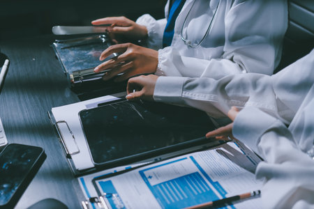 Two doctors and a female nurse meet at a table in the hospital, collaborating on medical tasks using...