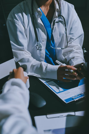 Two doctors and a female nurse meet at a table in the hospital, collaborating on medical tasks using laptops and computersの写真素材