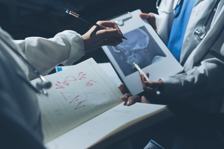 Two doctors and a female nurse meet at a table in the hospital, collaborating on medical tasks using laptops and computersの写真素材