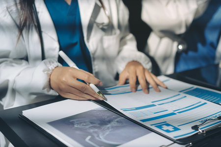 Two doctors and a female nurse meet at a table in the hospital, collaborating on medical tasks using laptops and computersの写真素材