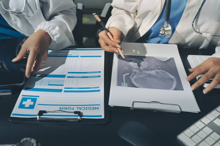 Two doctors and a female nurse meet at a table in the hospital, collaborating on medical tasks using laptops and computersの写真素材