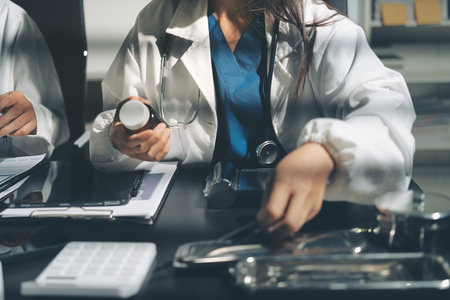 Two doctors and a female nurse meet at a table in the hospital, collaborating on medical tasks using laptops and computersの写真素材