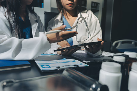 Two doctors and a female nurse meet at a table in the hospital, collaborating on medical tasks using...