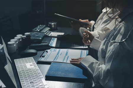 Two doctors and a female nurse meet at a table in the hospital, collaborating on medical tasks using laptops and computersの写真素材