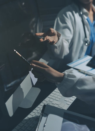 Two doctors and a female nurse meet at a table in the hospital, collaborating on medical tasks using laptops and computersの写真素材
