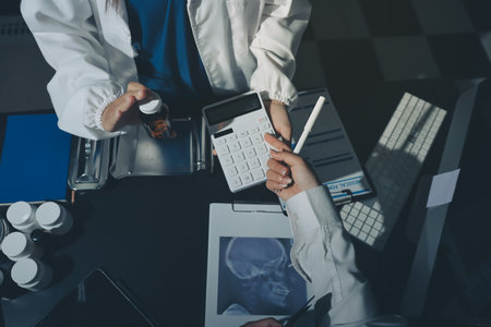 Two doctors and a female nurse meet at a table in the hospital, collaborating on medical tasks using laptops and computersの写真素材
