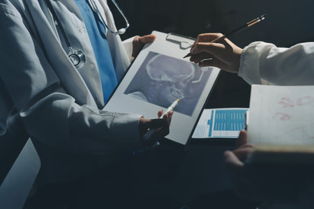 Two doctors and a female nurse meet at a table in the hospital, collaborating on medical tasks using laptops and computersの写真素材