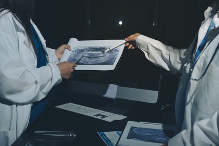 Two doctors and a female nurse meet at a table in the hospital, collaborating on medical tasks using laptops and computersの写真素材