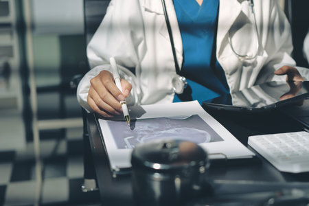 Two doctors and a female nurse meet at a table in the hospital, collaborating on medical tasks using laptops and computersの写真素材
