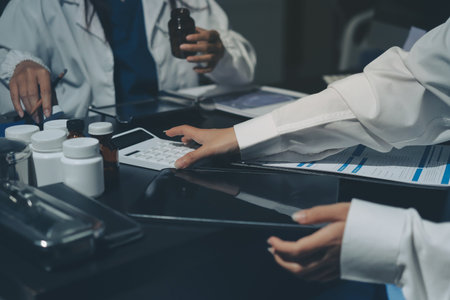 Two doctors and a female nurse meet at a table in the hospital, collaborating on medical tasks using laptops and computersの写真素材