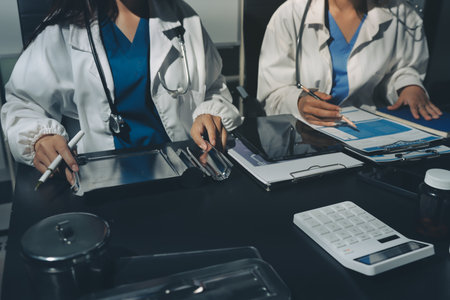 Two doctors and a female nurse meet at a table in the hospital, collaborating on medical tasks using laptops and computersの写真素材