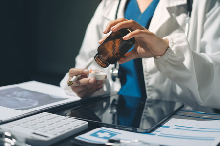Two doctors and a female nurse meet at a table in the hospital, collaborating on medical tasks using laptops and computersの写真素材