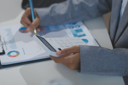 Asian Businesswoman Using laptop computer and working at office with calculator document on desk, doing planning analyzing the financial report, business plan investment, finance analysis concept.の写真素材