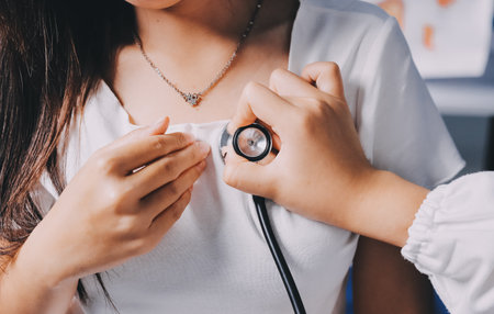 Doctor examining patient with stethoscope in hospital bed. Medical care and healthcare concept in a clinical setting.の写真素材