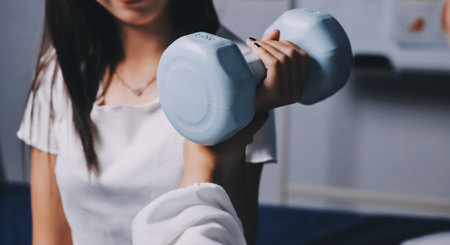 old woman training with physiotherapist using dumbbells at home therapist assisting senior woman with exercises in nursing home elderly patient using dumbbells with outstretched arms no logos no branの写真素材