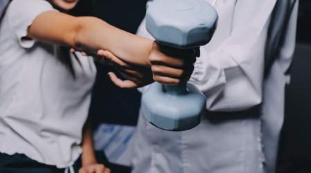 old woman training with physiotherapist using dumbbells at home therapist assisting senior woman with exercises in nursing home elderly patient using dumbbells with outstretched arms no logos no branの写真素材