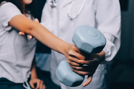 old woman training with physiotherapist using dumbbells at home therapist assisting senior woman with exercises in nursing home elderly patient using dumbbells with outstretched arms no logos no branの写真素材