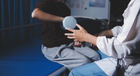 Old woman training with physiotherapist using dumbbells at home. Therapist assisting senior woman...