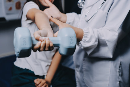 old woman training with physiotherapist using dumbbells at home therapist assisting senior woman with exercises in nursing home elderly patient using dumbbells with outstretched armsの写真素材