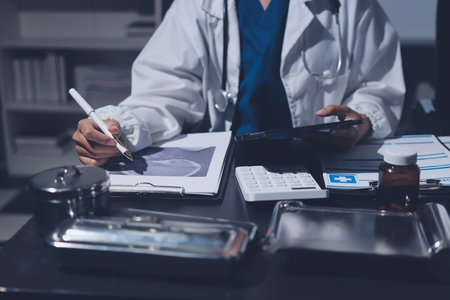 Two doctors and a female nurse meet at a table in the hospital, collaborating on medical tasks using laptops and computersの写真素材