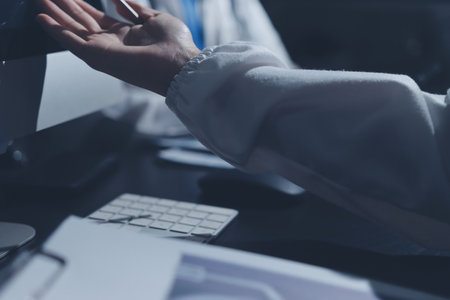 Two doctors and a female nurse meet at a table in the hospital, collaborating on medical tasks using laptops and computersの写真素材